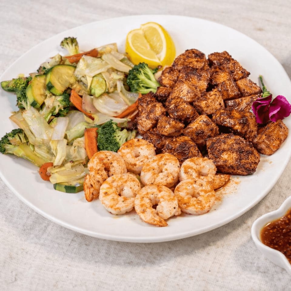 Grilled chicken, shrimp, and mixed vegetables with a lemon wedge and purple flower garnish.