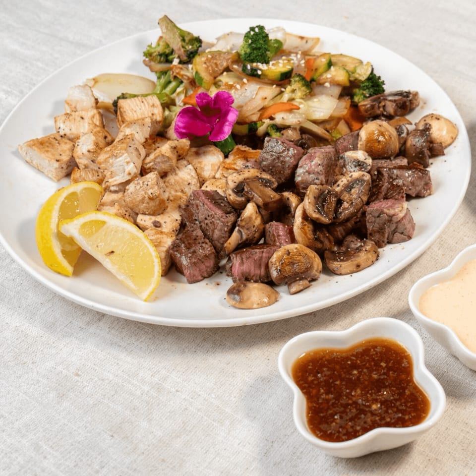 Hibachi chicken and steak with mushrooms, mixed vegetables, lemon wedges, and two dipping sauces.